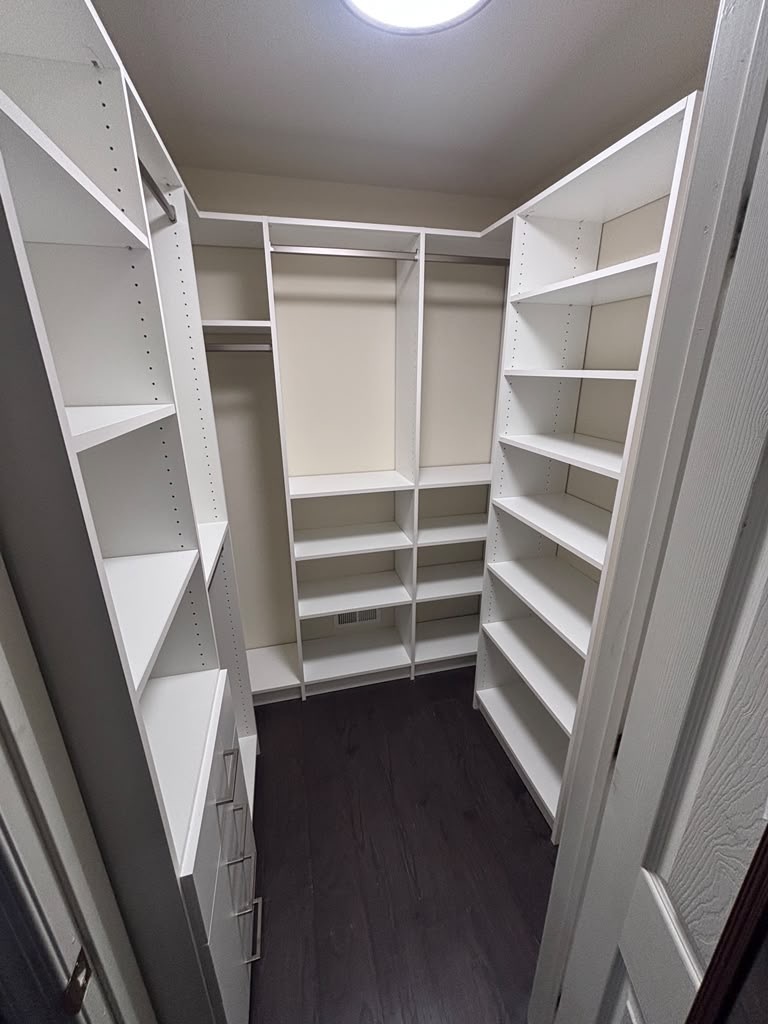 Compact L-shaped walk-in closet with full-height shelving and hanging sections
