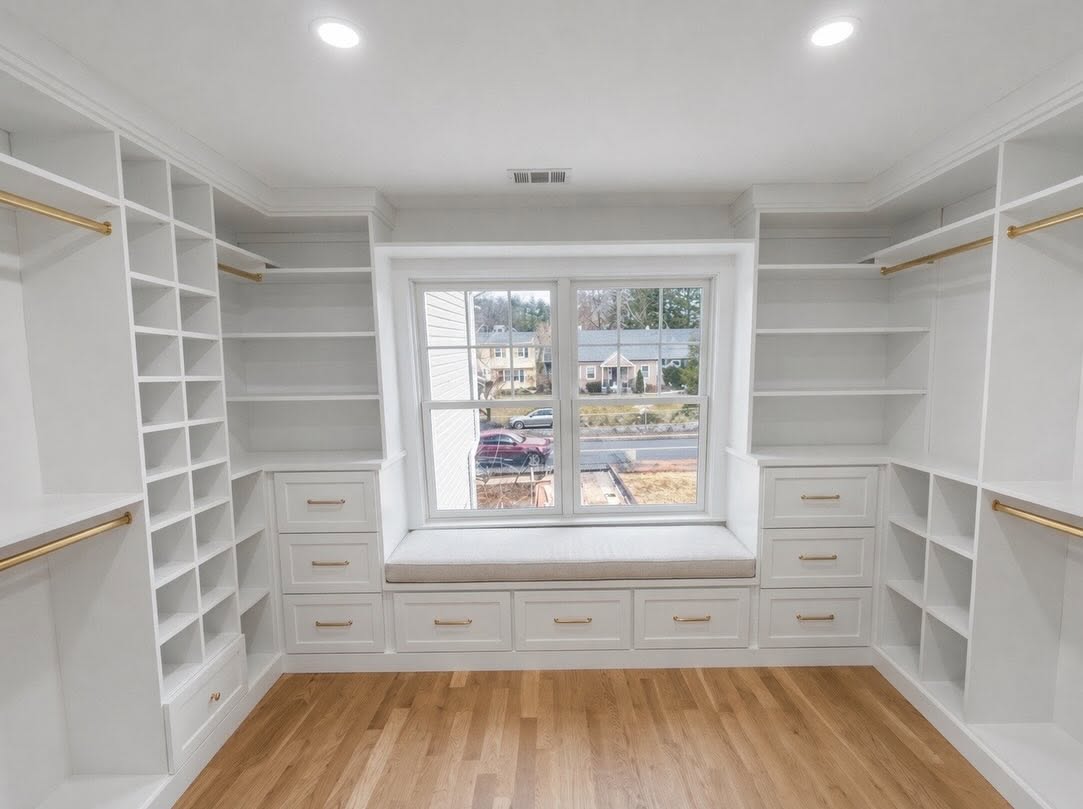 Custom walk-in closet in a New Jersey home with window seat, brass hanging rods and full-height shelving