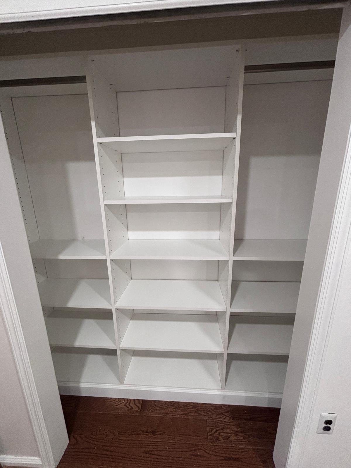 Reach-in closet with a full-height shelving tower above hardwood flooring